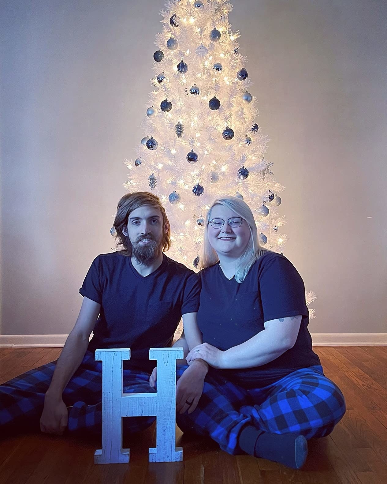Two reviewers wearing matching blue plaid PJ pants posing in front of Christmas tree decoration