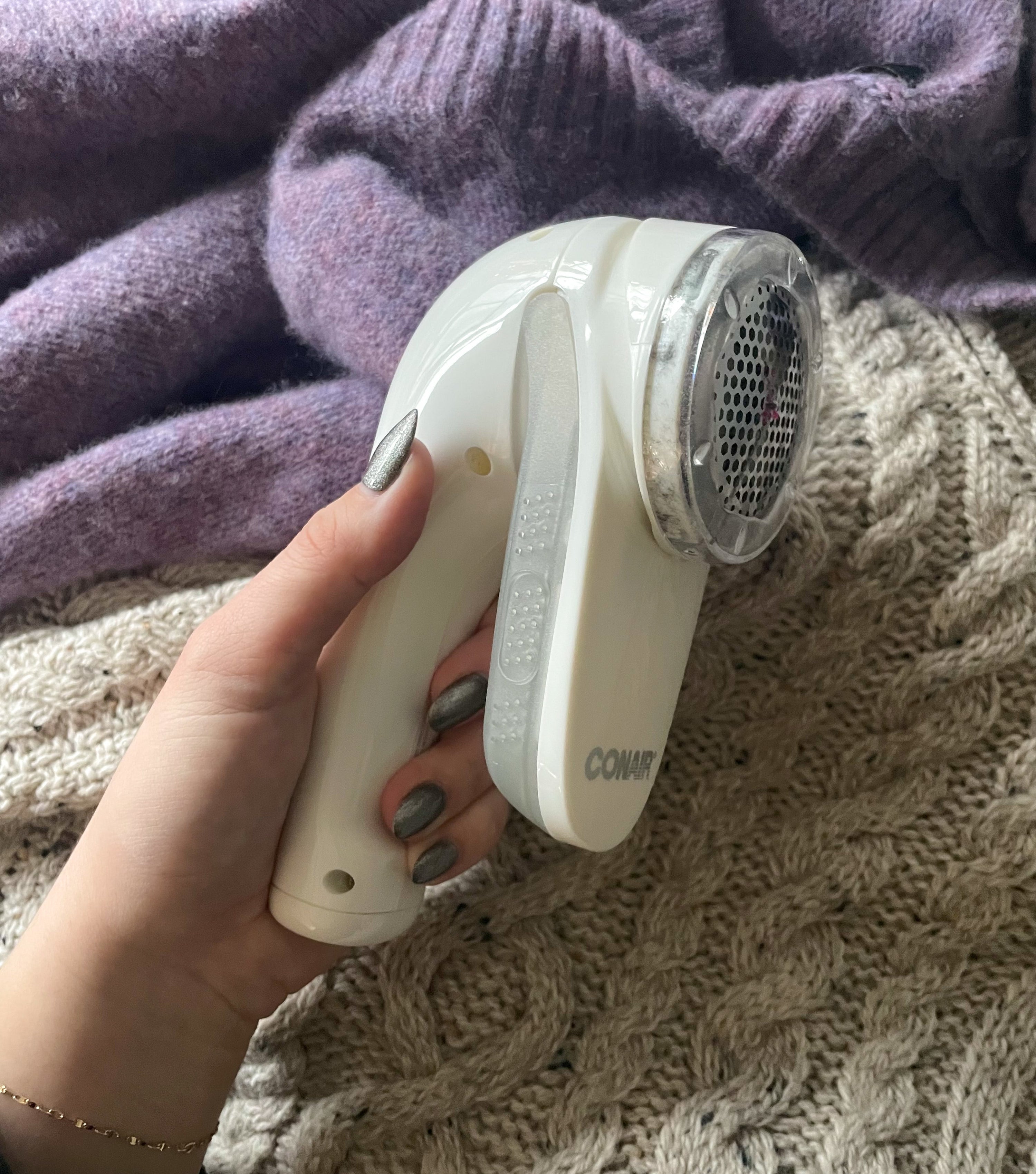 victoria holding up the fabric shaver against a pair of sweaters
