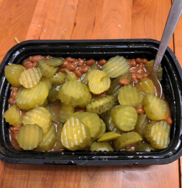 sliced pickles and canned beans mixed together in a plastic takeout container
