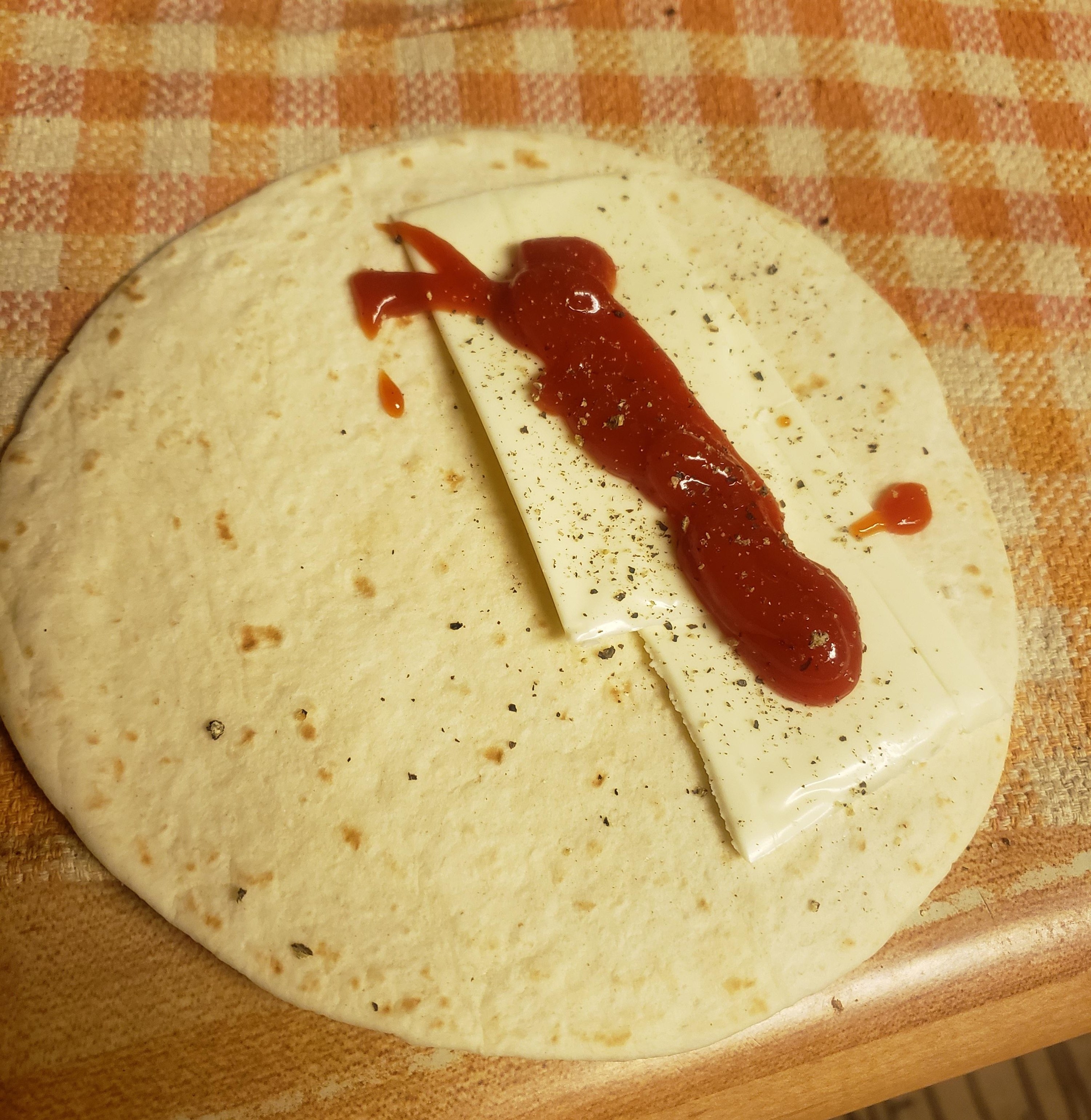 A tortilla with sliced white cheddar, a splat of ketchup, and pepper