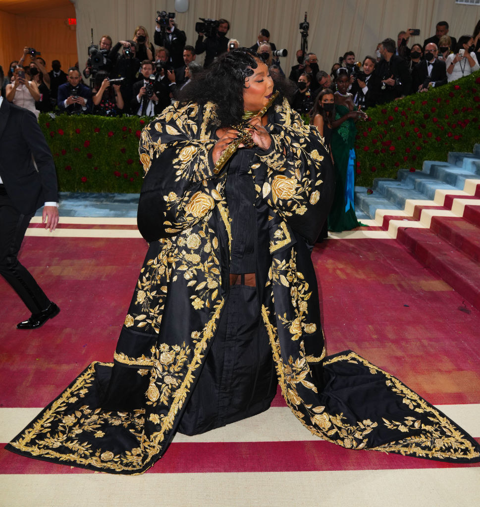 Lizzo in a gown with an ornate robe and playing the flute
