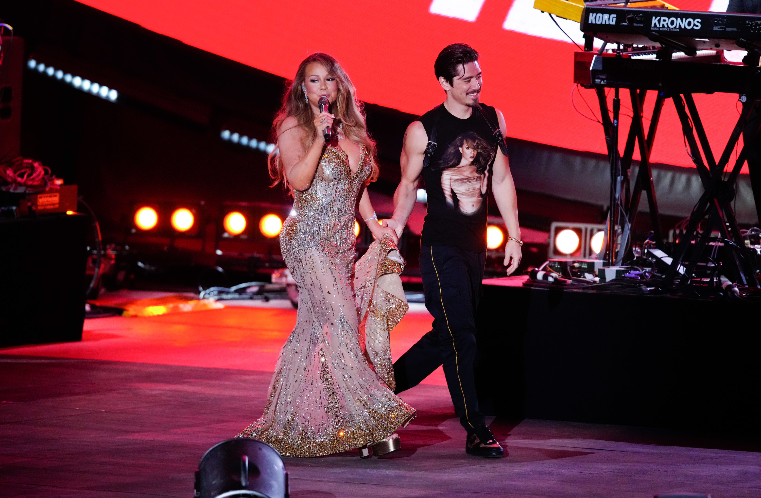Mariah Carey holding a mic and holding hands with Bryan Tanaka