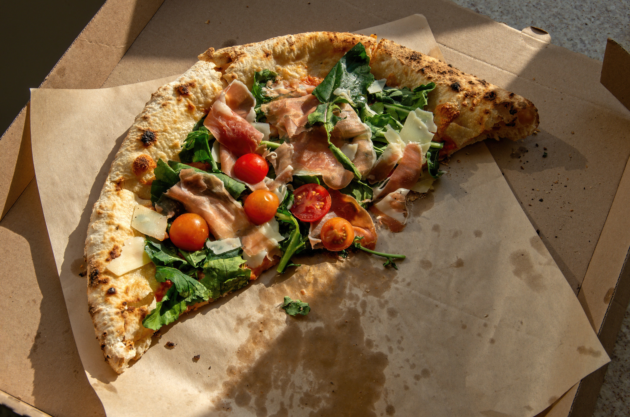 Sourdough pizza with prosciutto, arugula, and tomato.