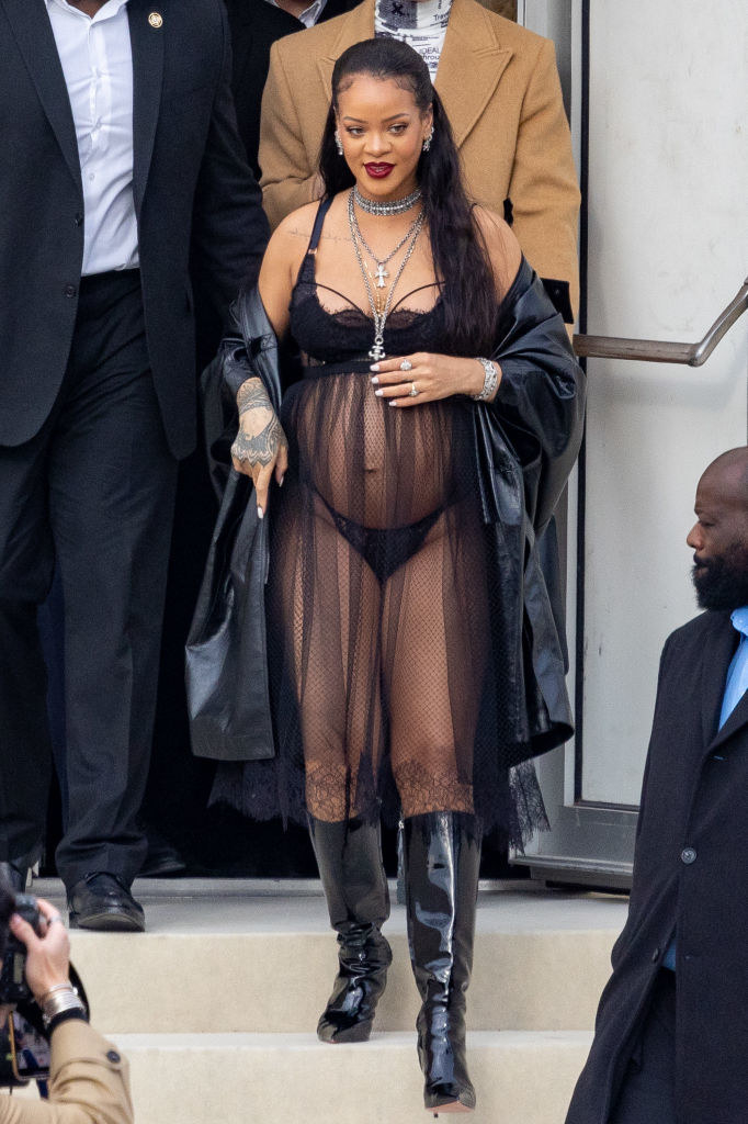 Rihanna wearing many necklaces and a sheer baby doll dress with bra and panties, coat, and knee-high boots