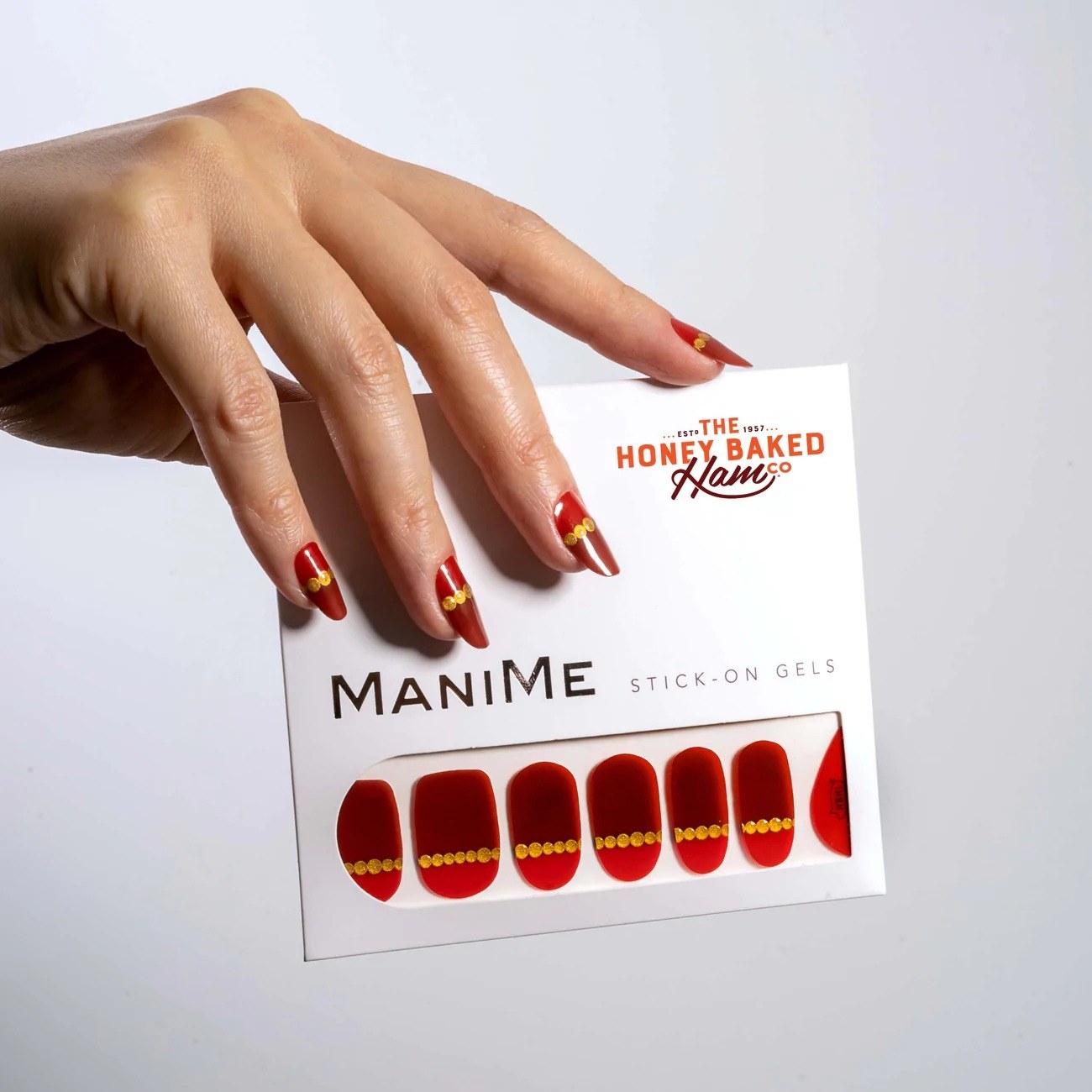 A manicured hand with the stick-on gels: red and burgundy with a horizontal gold dot line