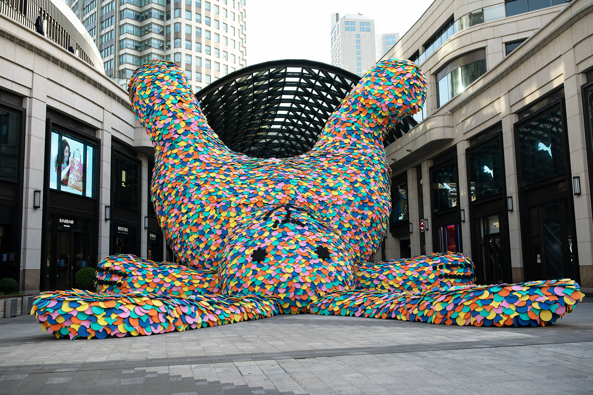 a gigantic rainbow sprinkle rabbit statue lying on its back in the corner of a mall