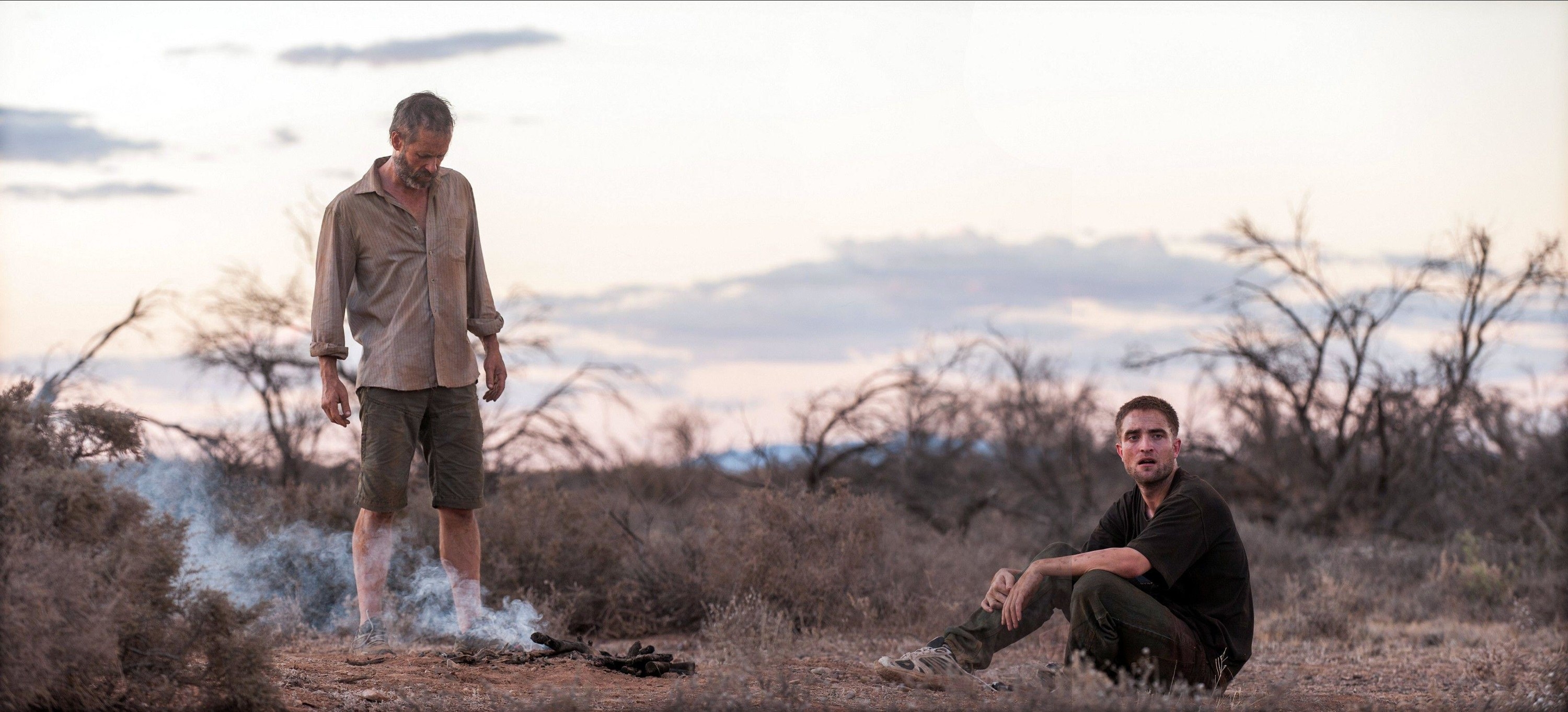 Two men stand in a desert near sundown near a dismal fire