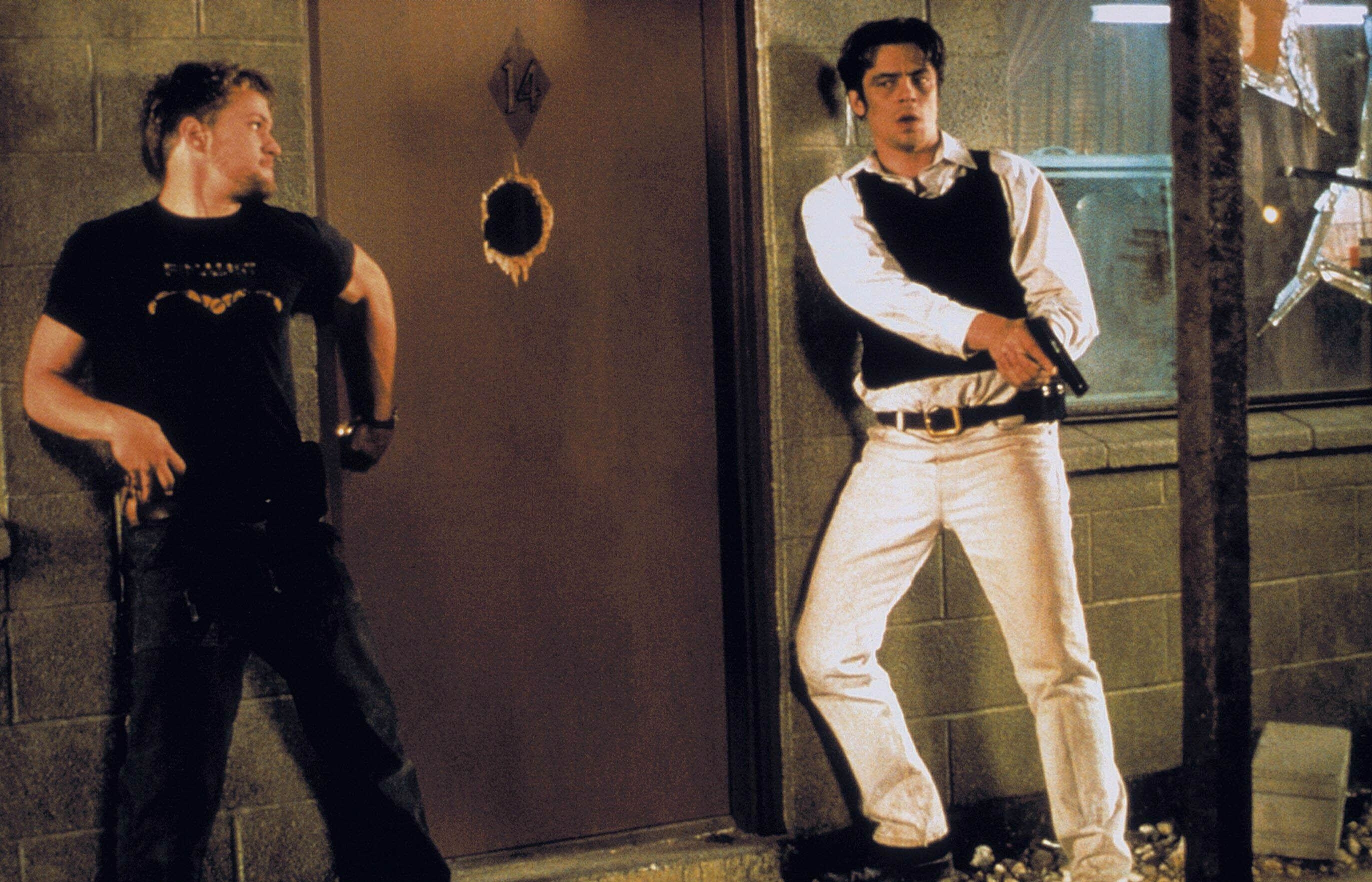Two tense young men stand next to a motel room door with a gaping bullet hole in its center