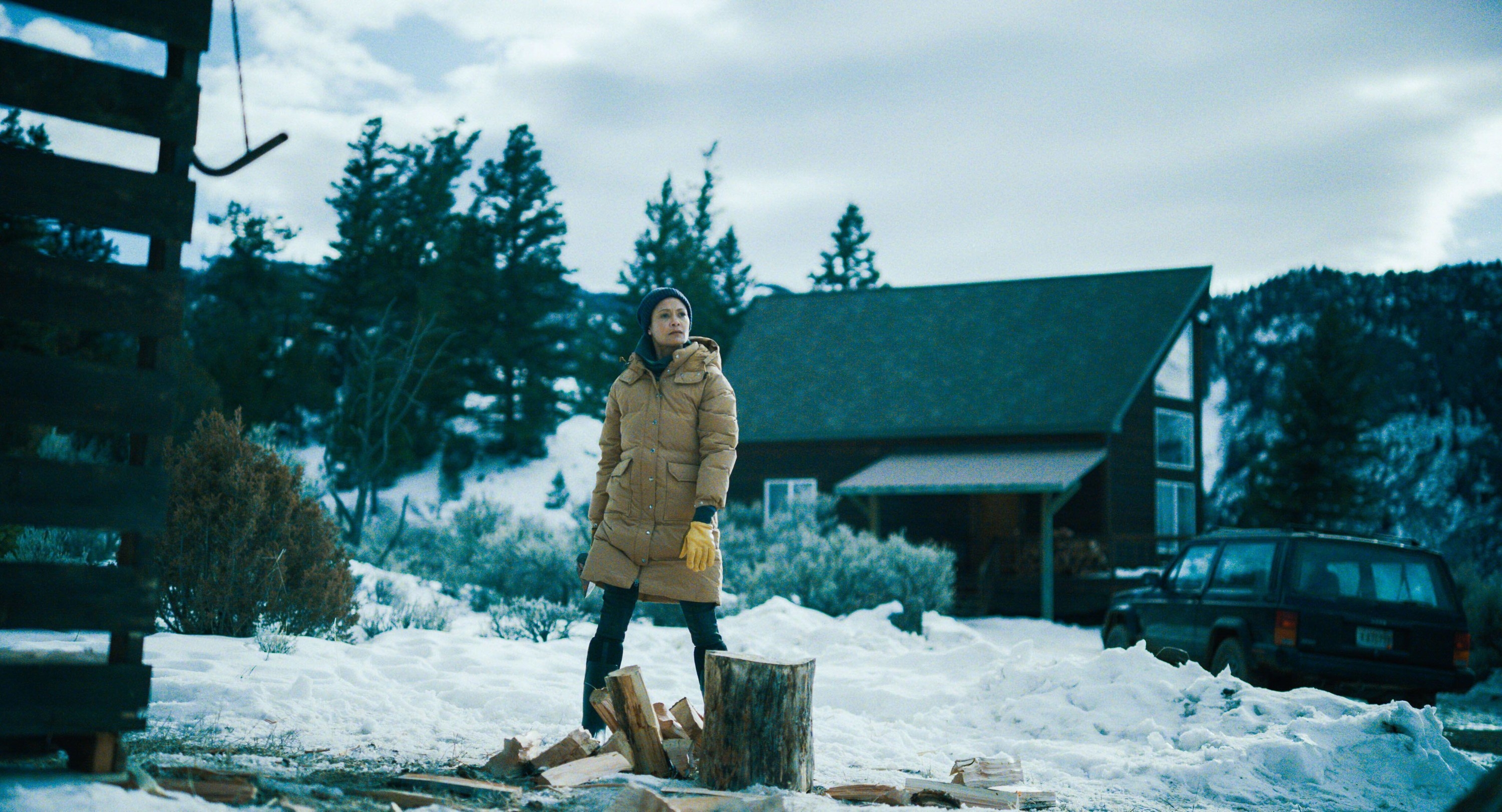 A woman stares off after cutting wood on a stump in the snow