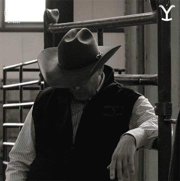 A man in a cowboy hat raises his hand in a horse stall