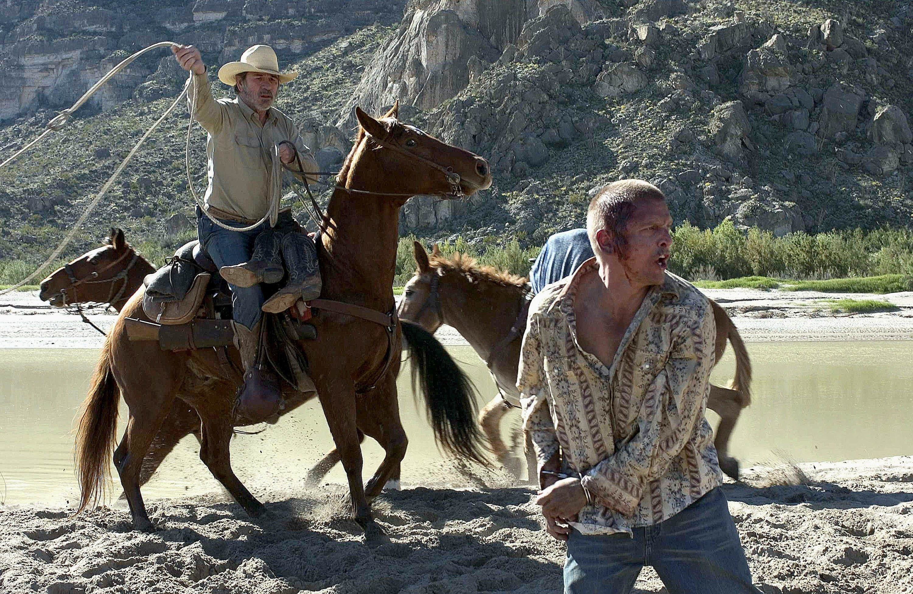 A bloodied man attempts to run from a cowboy on a horse with a lasso