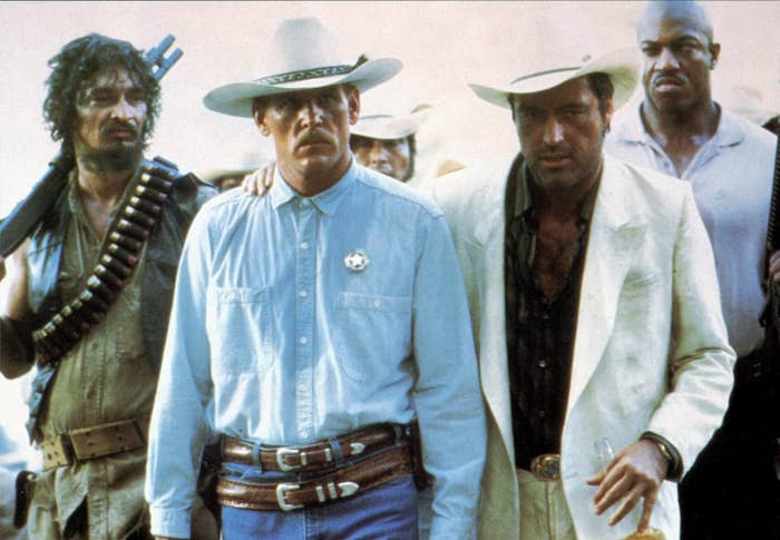 A sheriff in a cowboy hat is escorted by a number of shady criminals