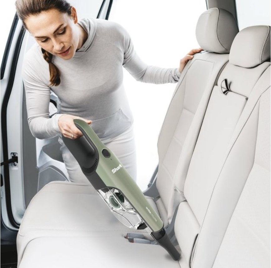 A model is holding a green vacuum to a car&#x27;s upholstery