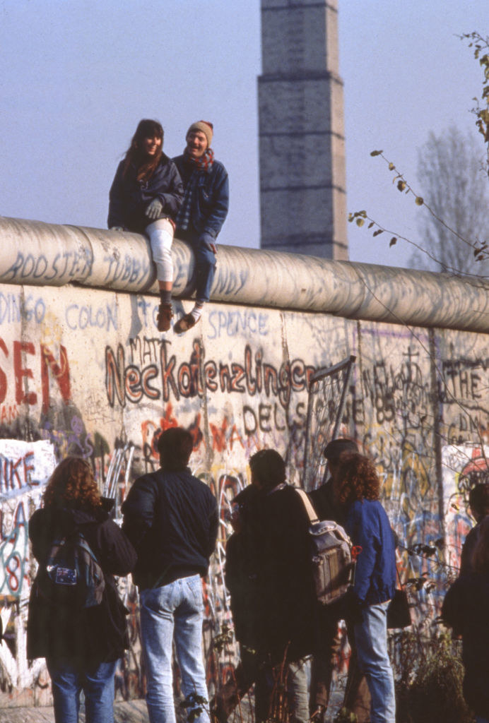 Smiling couple sitting on top of the Berlin Wall