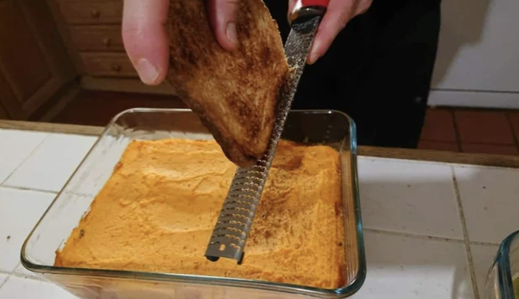 a person grating toast on a casserole