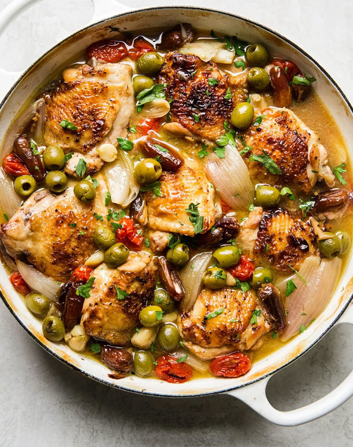 Chicken with olives, shallots, and tomato in a pan.