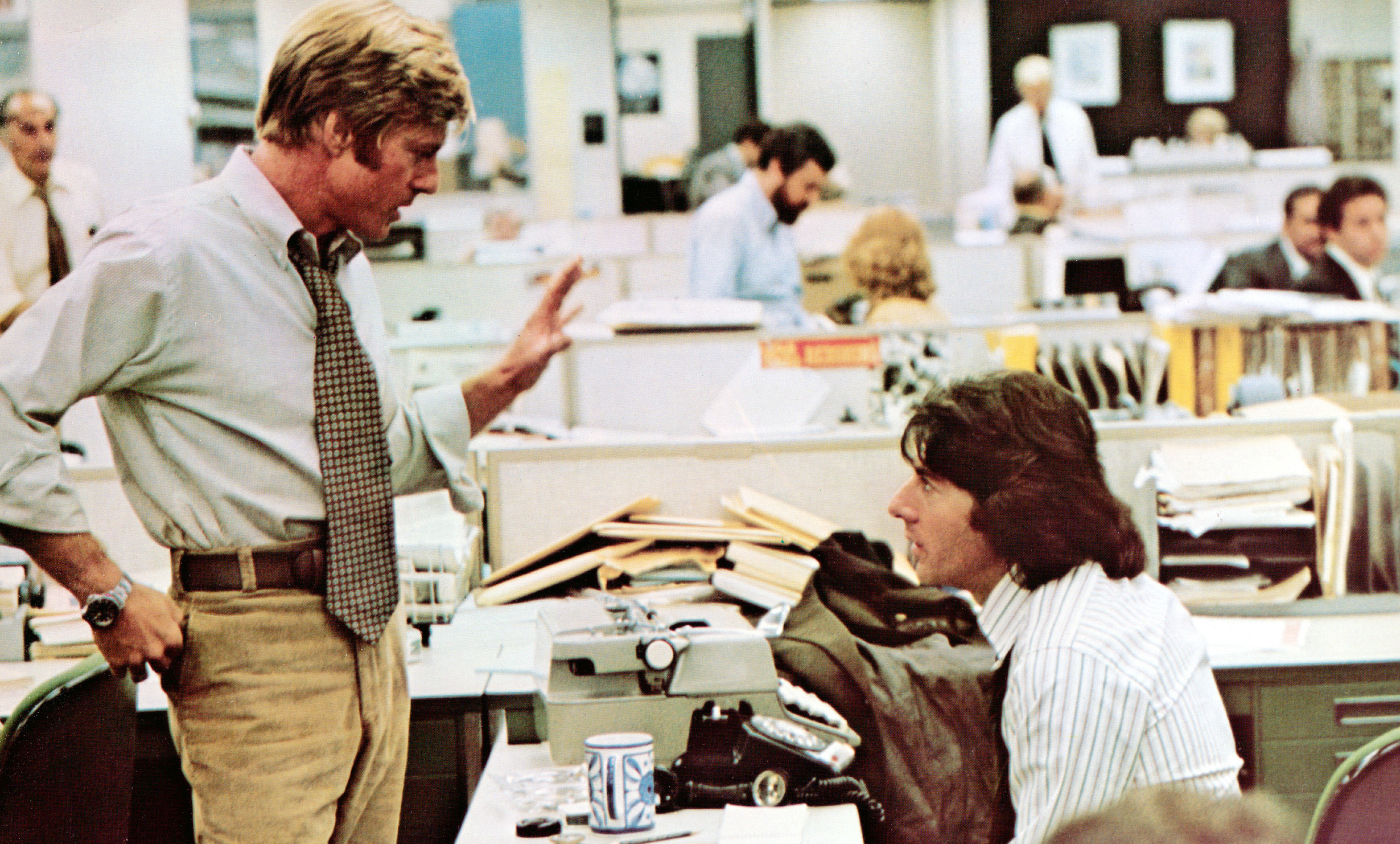 Robert Redford and Dustin Hoffman talking at a desk.