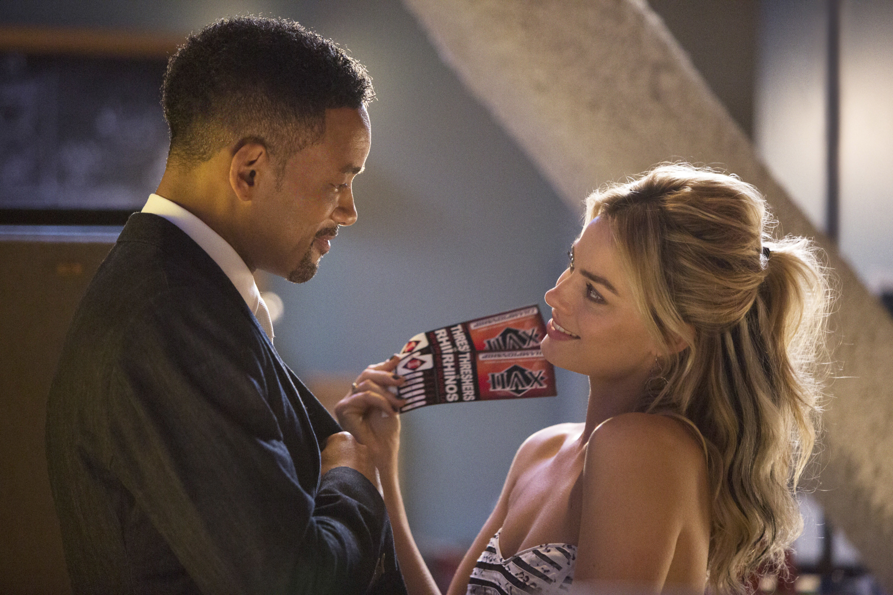 Margot Robbie holds two tickets next to Will Smith