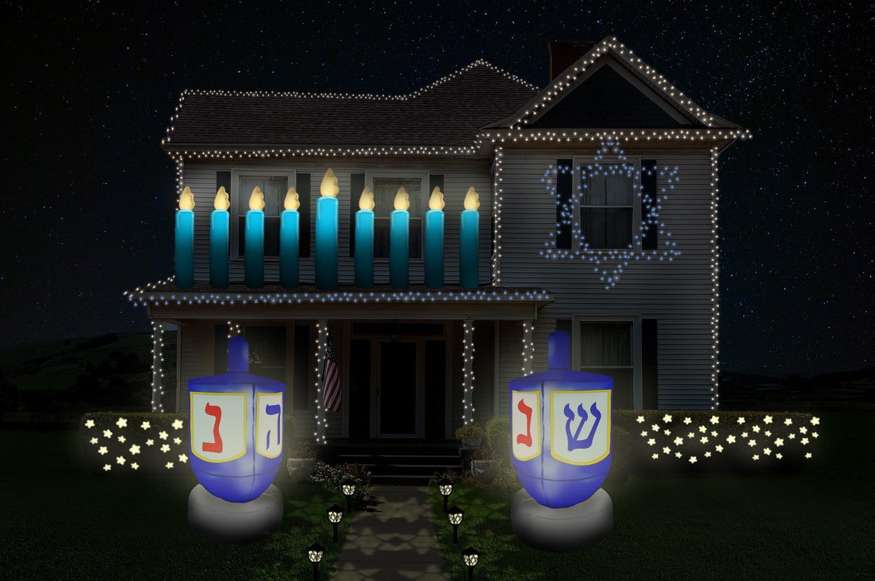 a house decked out in Hanukkah decorations. There are string lights, some in the shape of a Star of David, inflatable dreidel and menorah, and festive star shaped lights on the bushes.