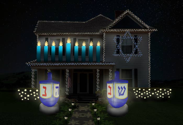 a house decked out in Hanukkah decorations including string lights, some in the shape of a Star of David, inflatable dreidel and menorah, and festive star-shaped lights on the bushes