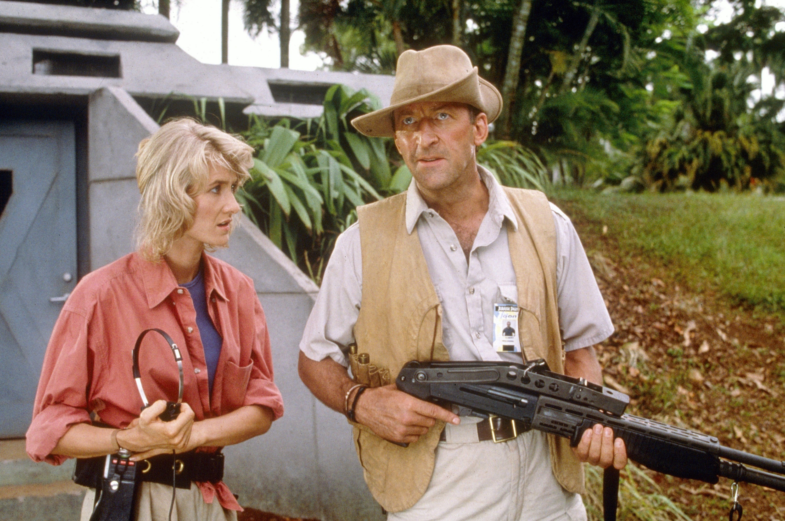 Laura Dern holding headphones and looking at Bob Peck, who&#x27;s holding a large weapon