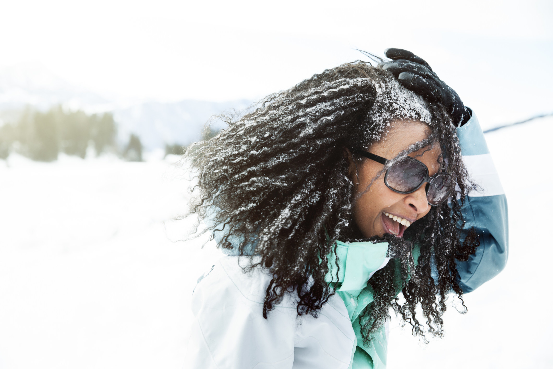 Woman wearing sunglasses holds down hair that blows in snowy wind