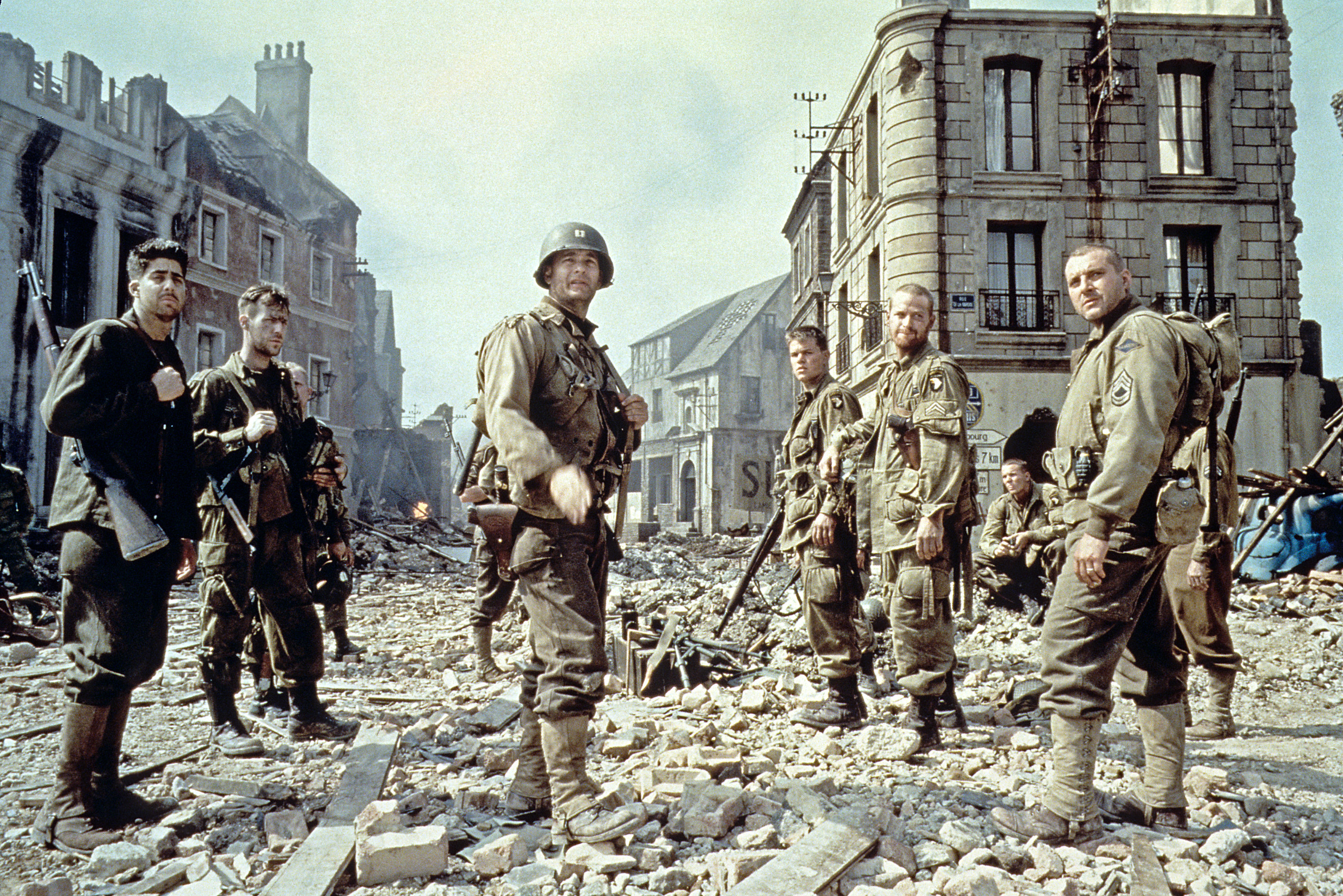 Men in military uniform standing amid rubble