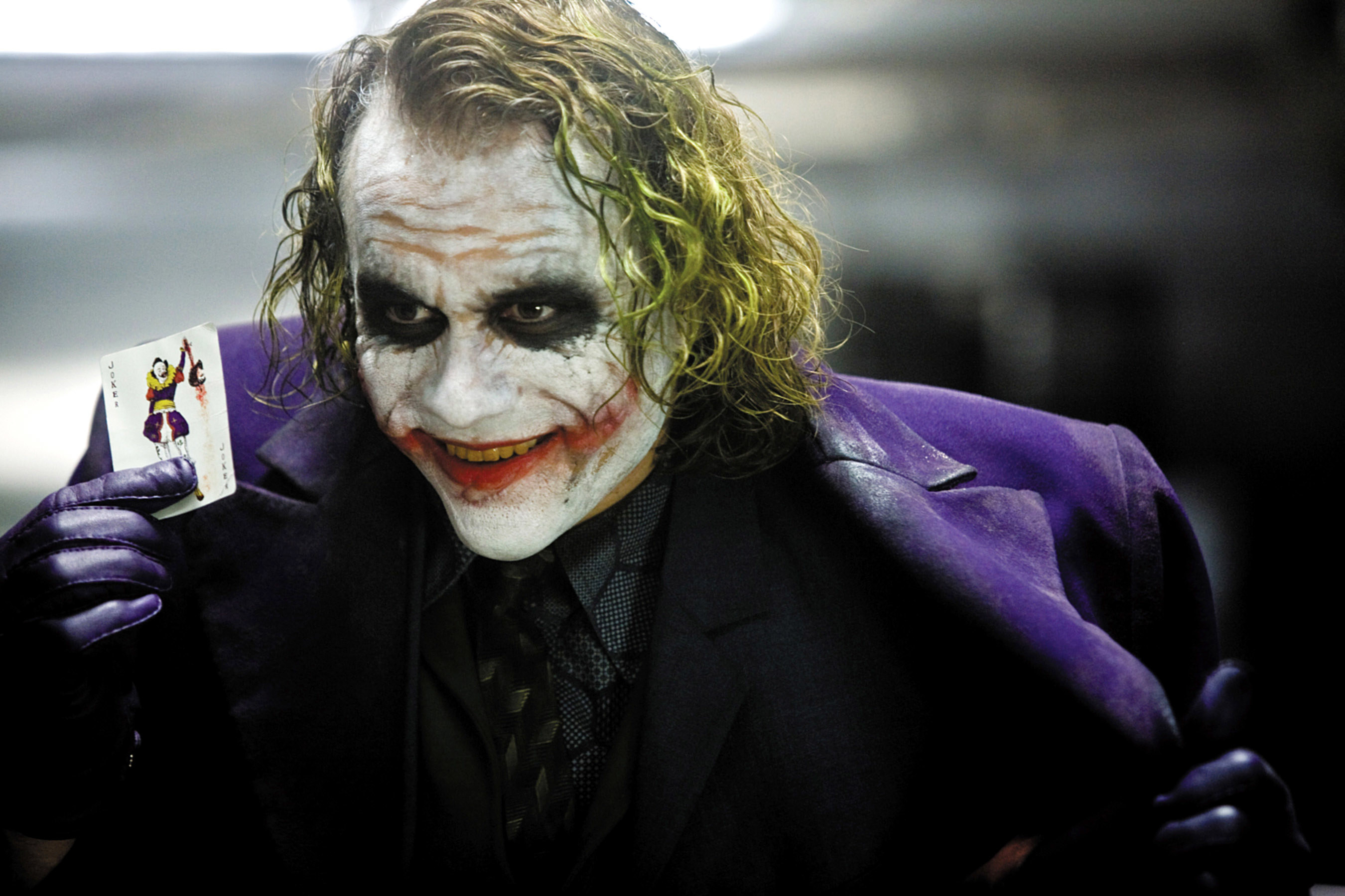 Heath Ledger as the Joker holding up a Joker card