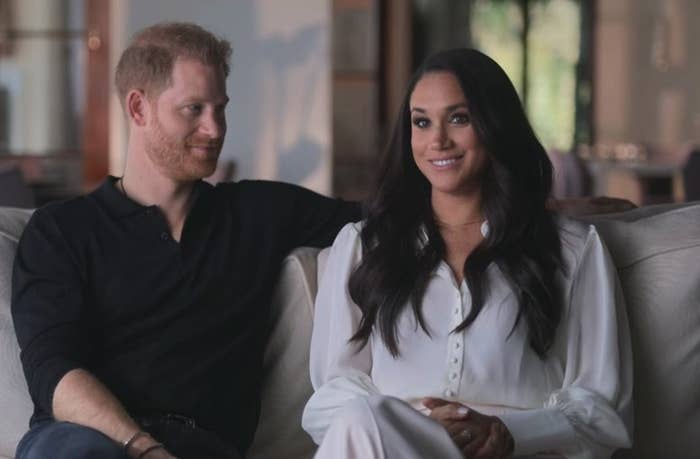 prince harry and meghan markle smiling and sitting on a sofa