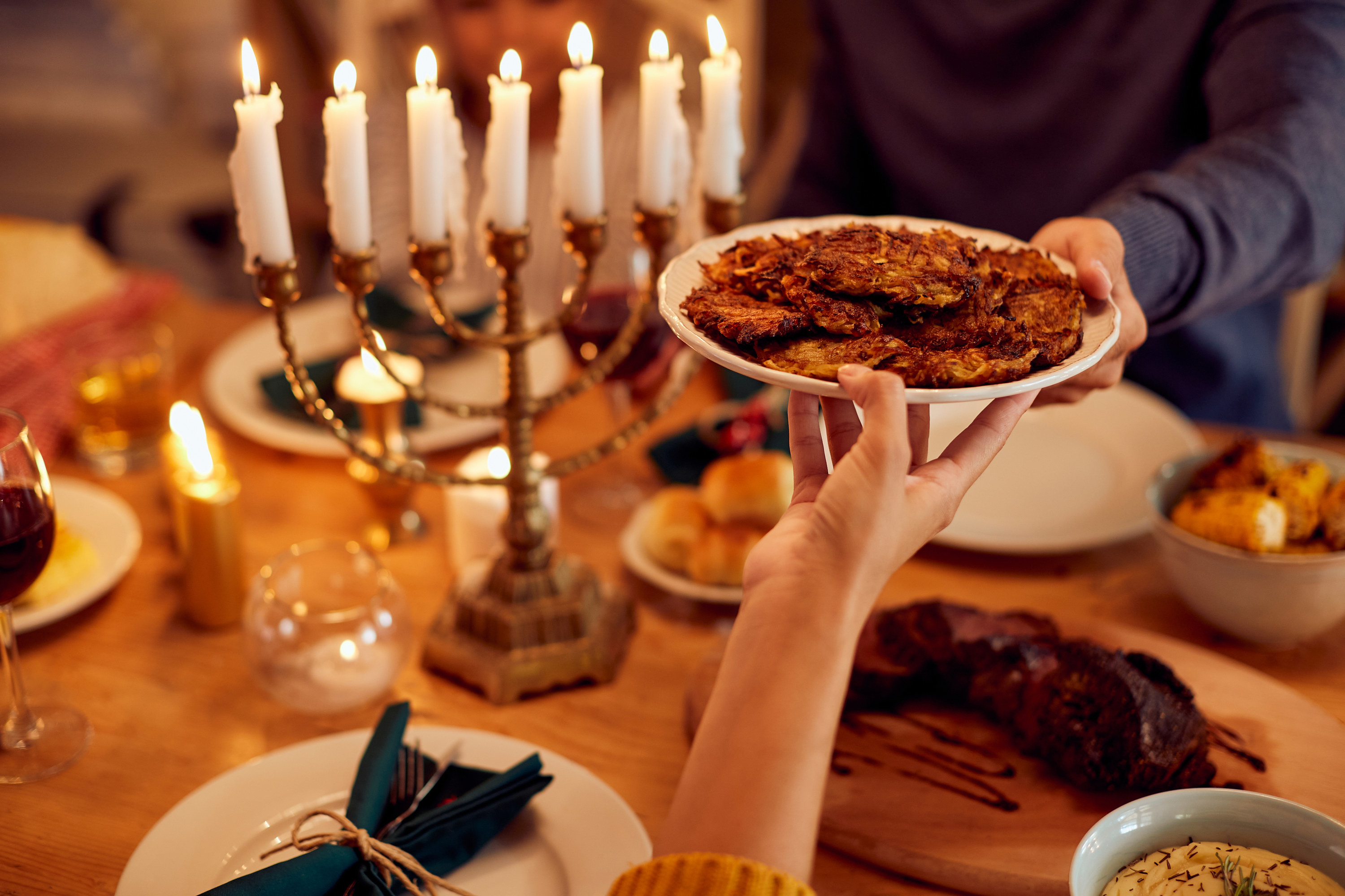 Close-up of couple passing latkes during a meal at dining table while celebrating Hanukkah at home