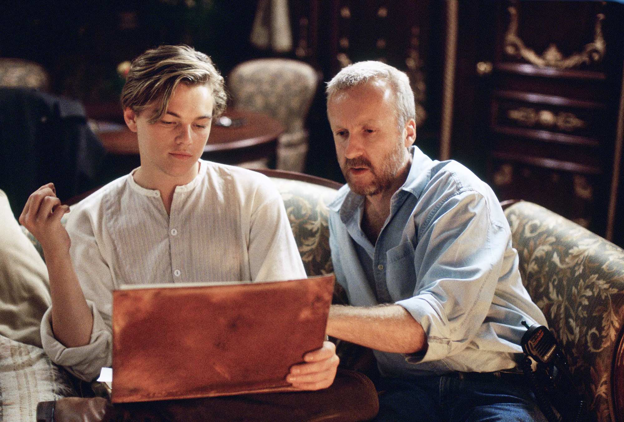  DiCaprio and Cameron sitting on a sofa looking at a book 