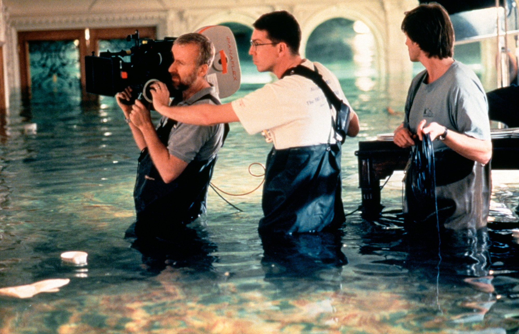 Cameron holding a large camera with crew in water during a flooding scene 