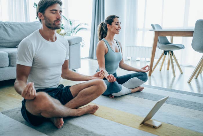 Beautiful young couple sitting on the floor and practicing yoga. Sporty couple using digital tablet for online yoga lessons