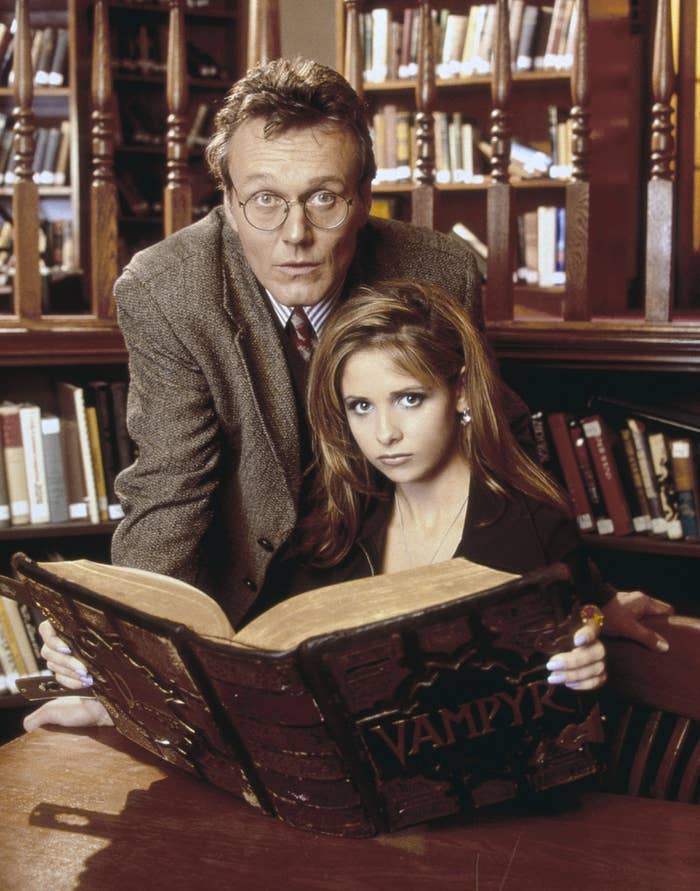buffy behind a large book while an older man stands behind her