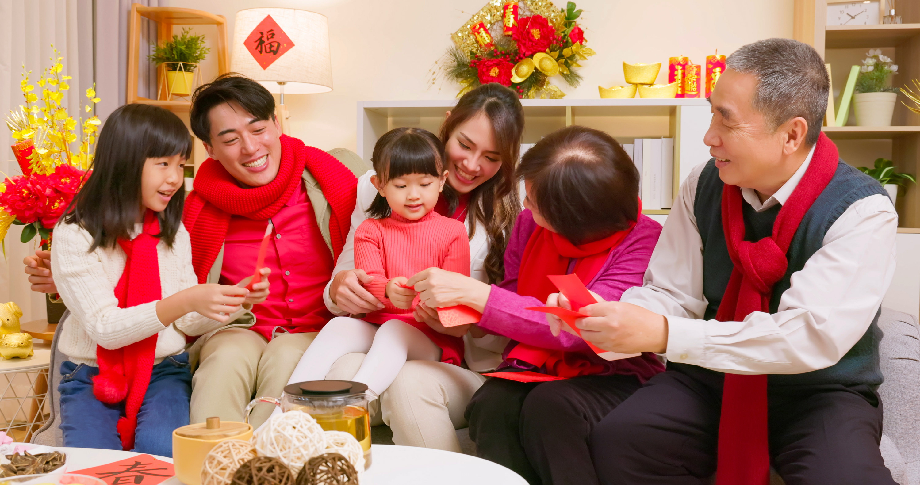 elderly couple grandparent giving red envelope lucky money to granddaughters and wishing them happy new year with hand gestures in living room