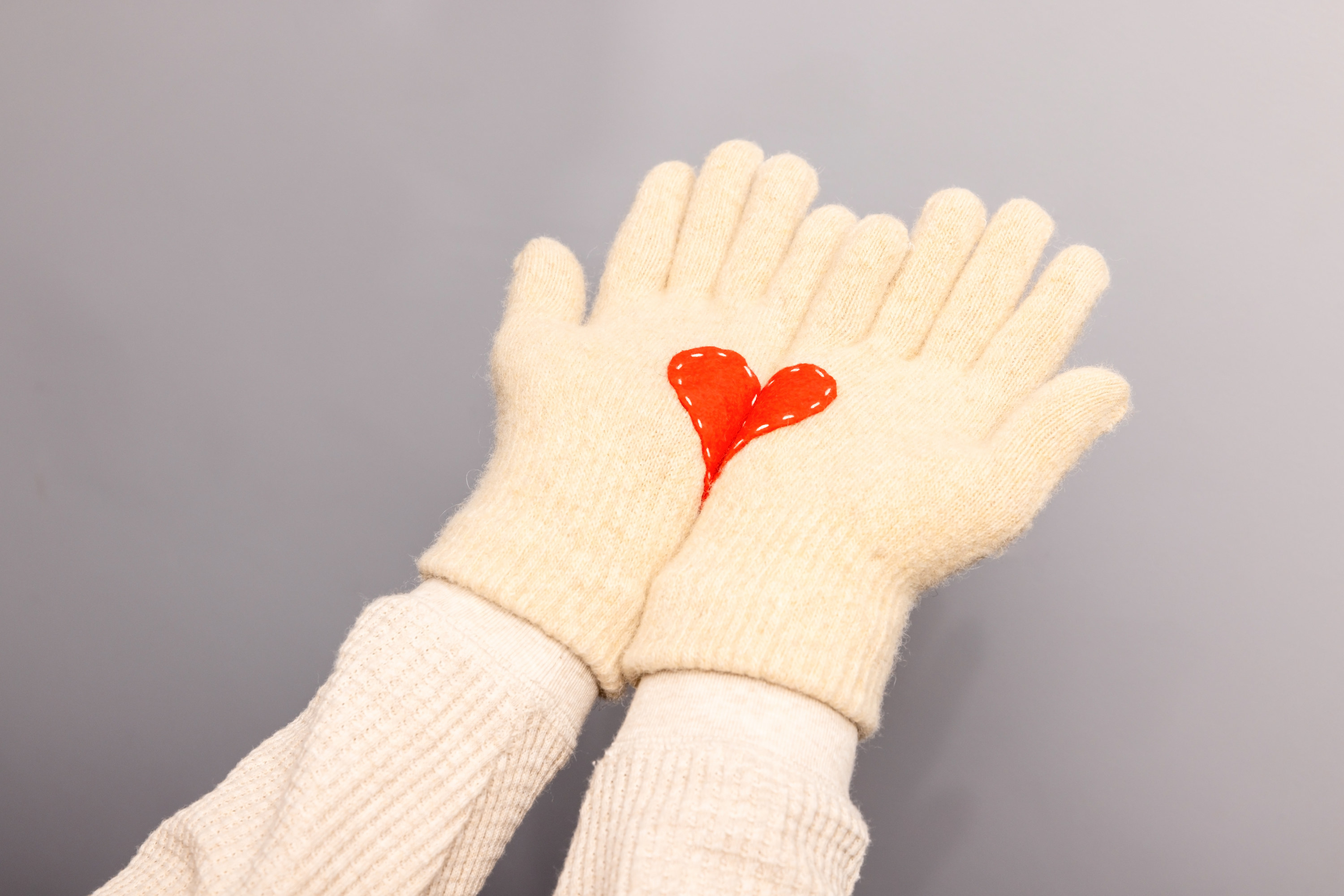 Woman hands in white knitted gloves with red heart