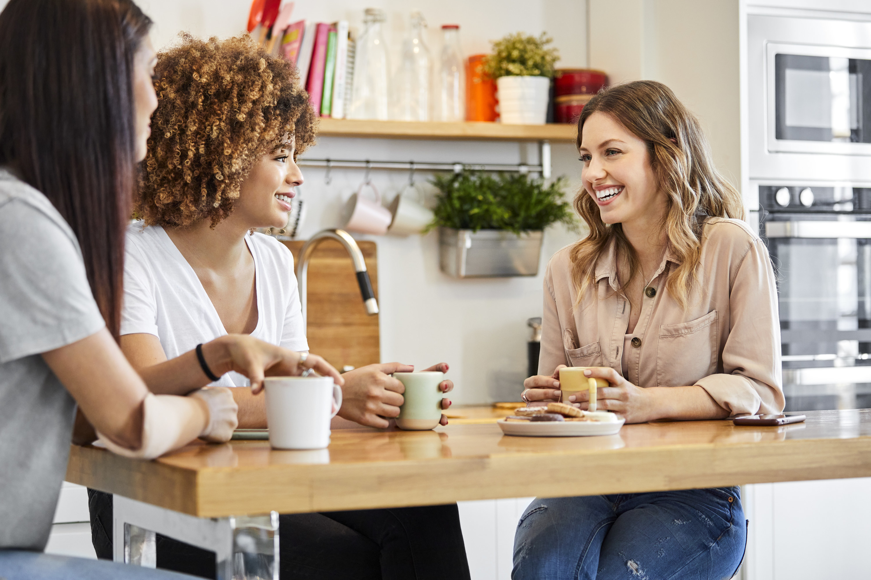 Young women listening to smiling friend while having coffee. Females are working at home. They are spending leisure time together