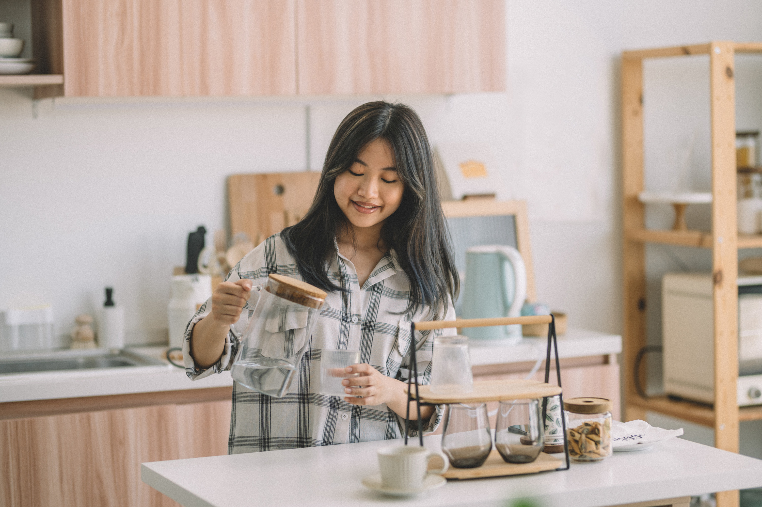Young Asian woman happily pouring water in drinking glass at kitchen