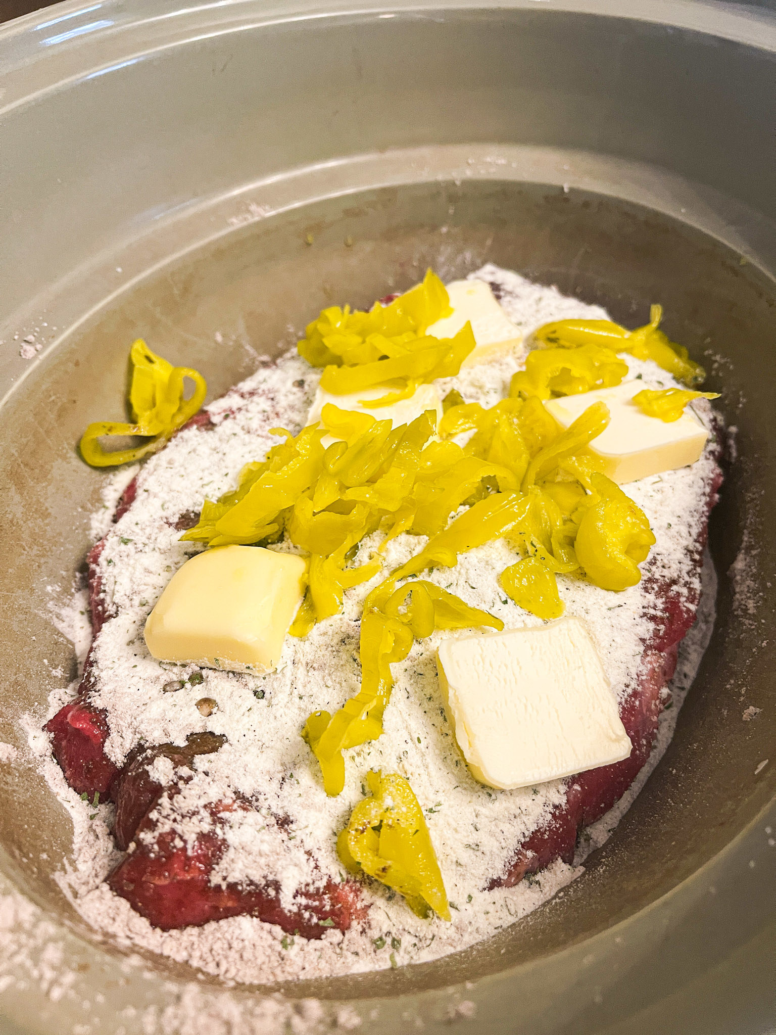 butter, pepperoncini peppers, and sauce mixes on top of roast in crock pot