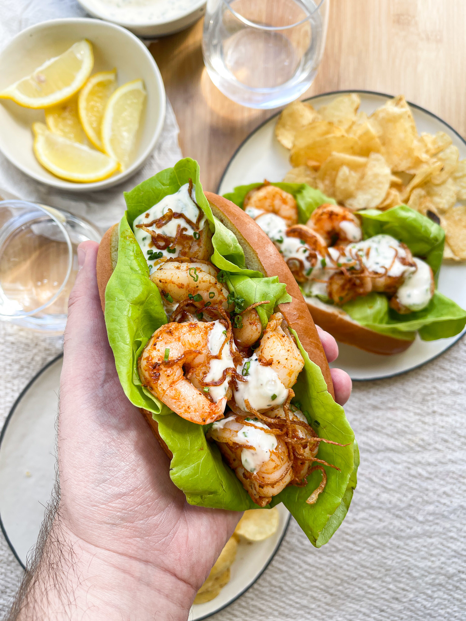 author holding up a shrimp roll with sauce, fried onions, and lettuce