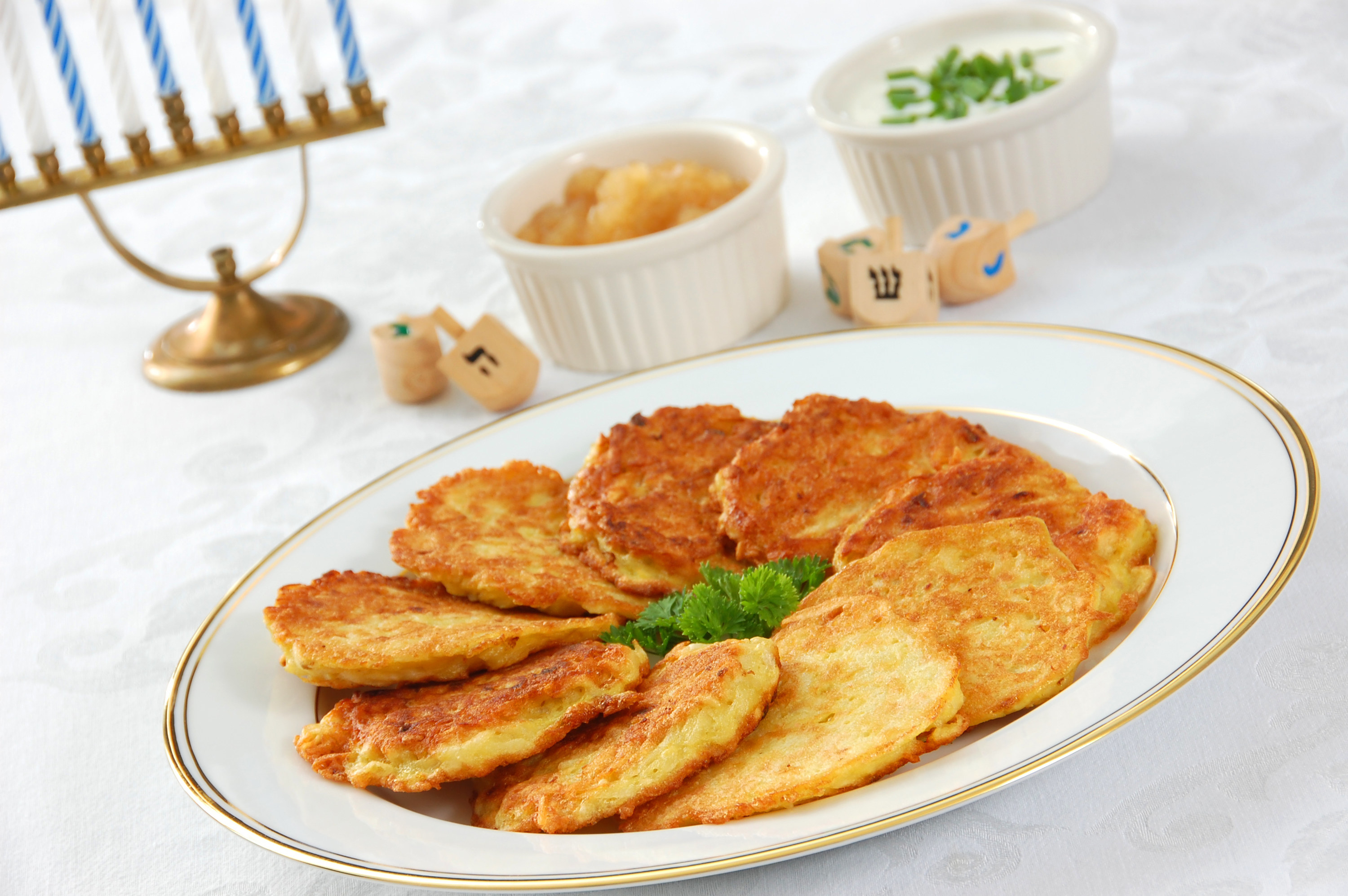 A table set for Hanukkah, with dreidels, menorah, and a plate of crispy latkes (potato pancakes) served with apple sauce and sour cream