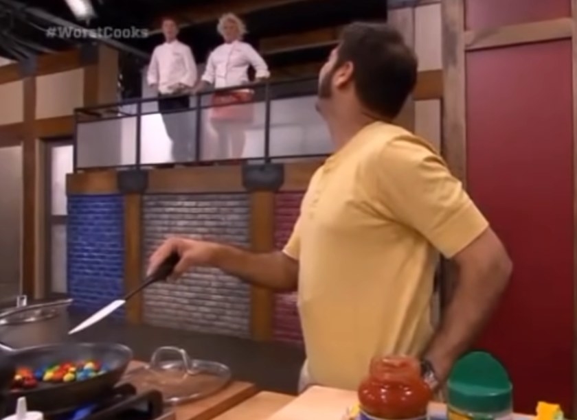 A contestant looking back at chefs Bobby Flay and Anne Burrell explaining his dish