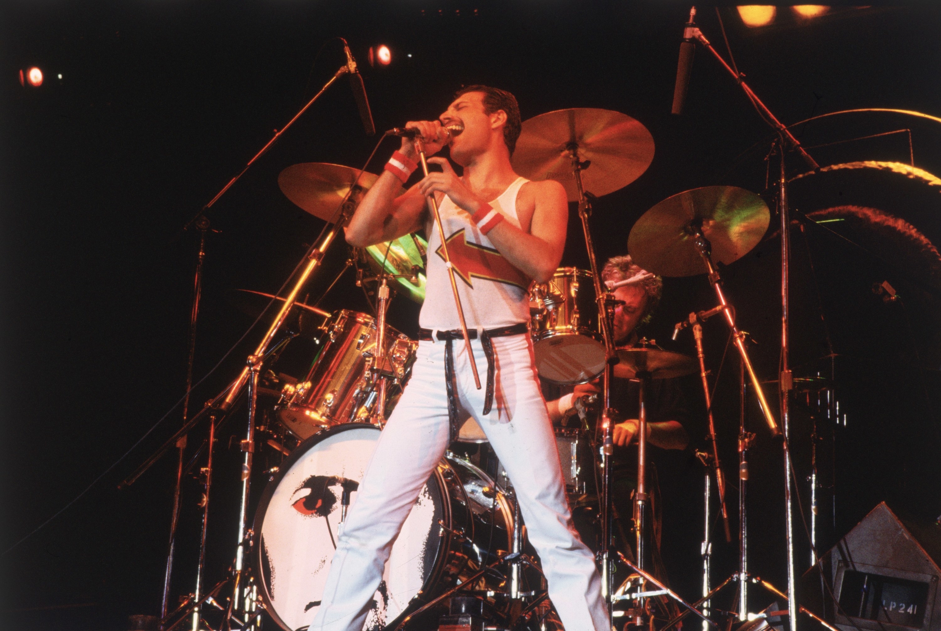Freddie Mercury performing in an all white outfit, belting into a microphone