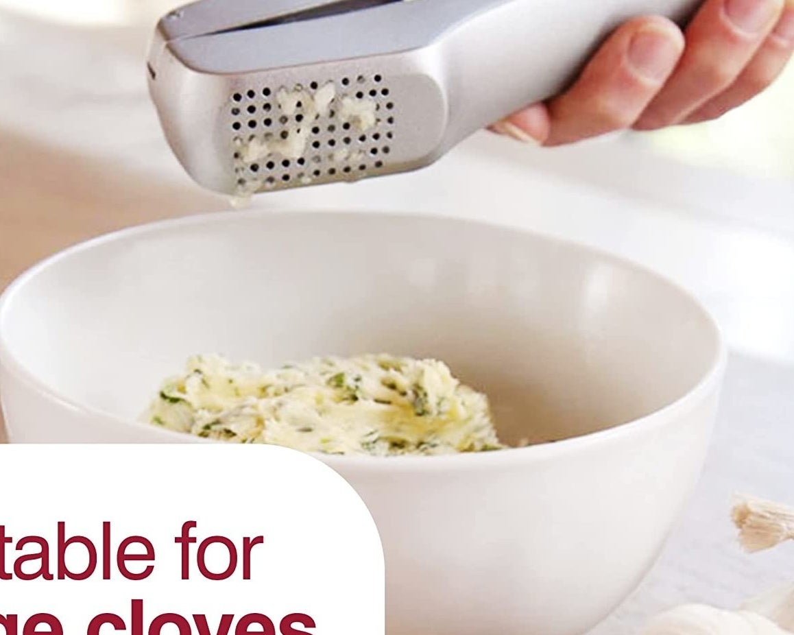 a person squeezing garlic into a bowl using the garlic press