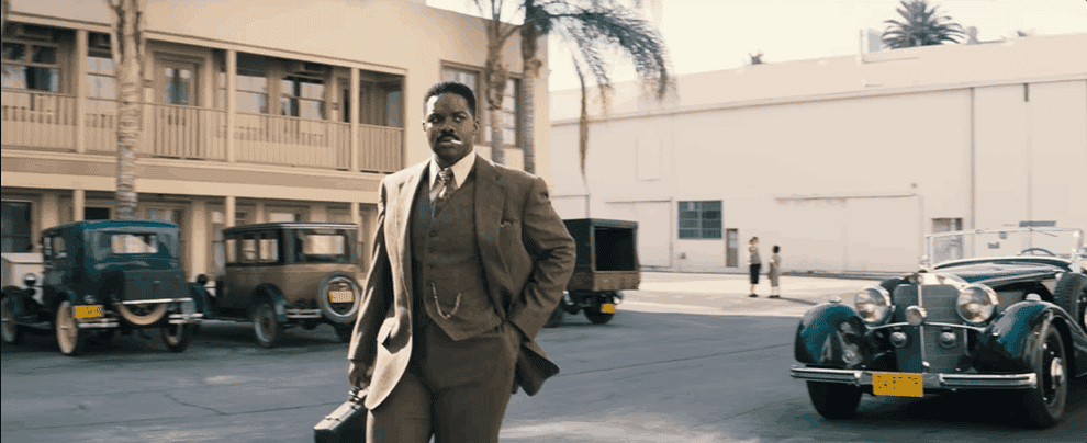 Movie gif: Jovan Adepo wearing a brown three-piece suit on a studio lot