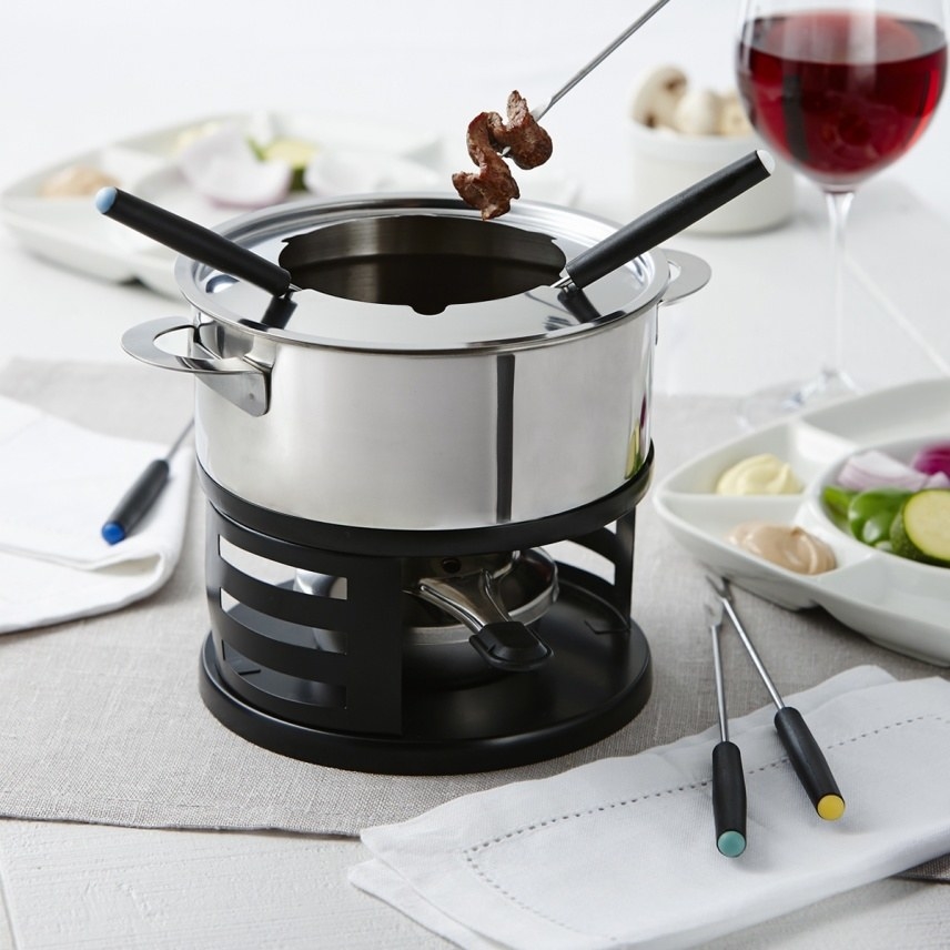 The fondue set on a table with glasses, plates, and a tray dips and veggies
