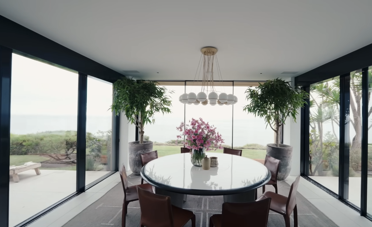 formal dining room with large circular table and flowers surrounded by large windows