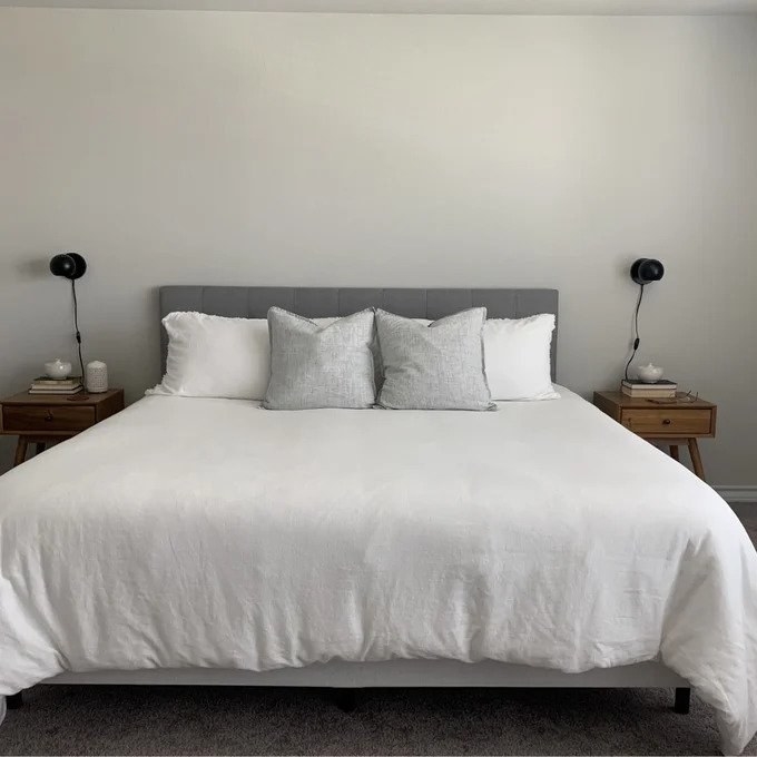 a reviewer photo of the gray headboard behind bed with white comforter and white and gray pillows