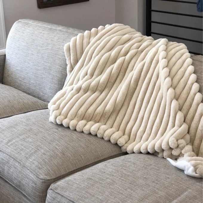 a reviewer photo of the beige throw blanket on a gray couch