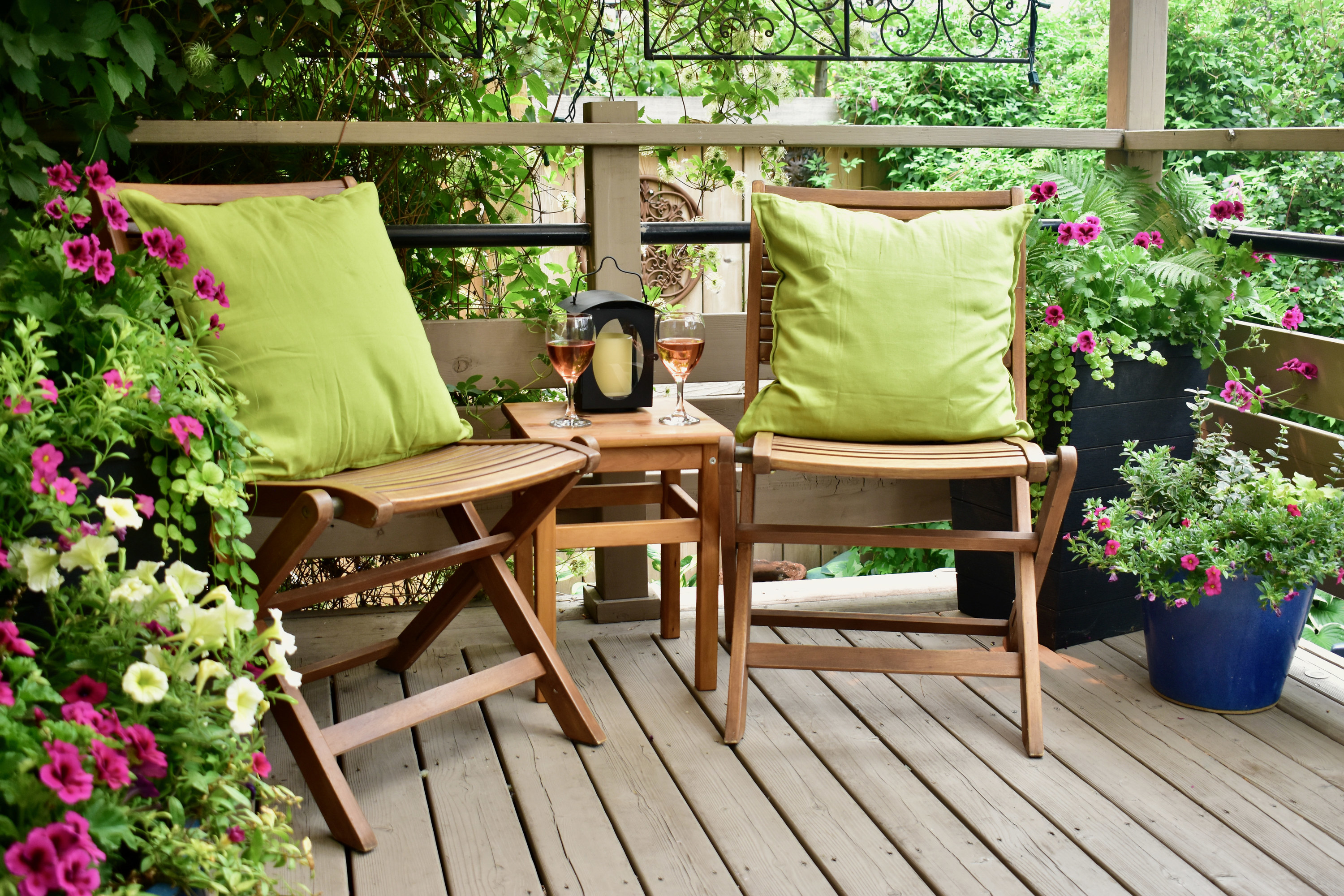 deck decorated with plants chairs a table and wine glasses